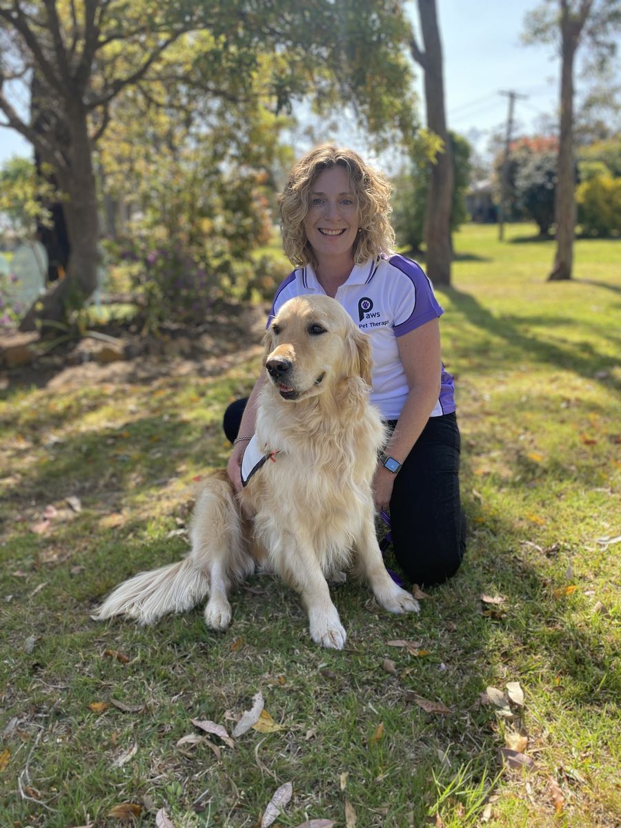 PAWS volunteer Alison kneeling beside Luna, her golden retriever therapy dog, on the grass