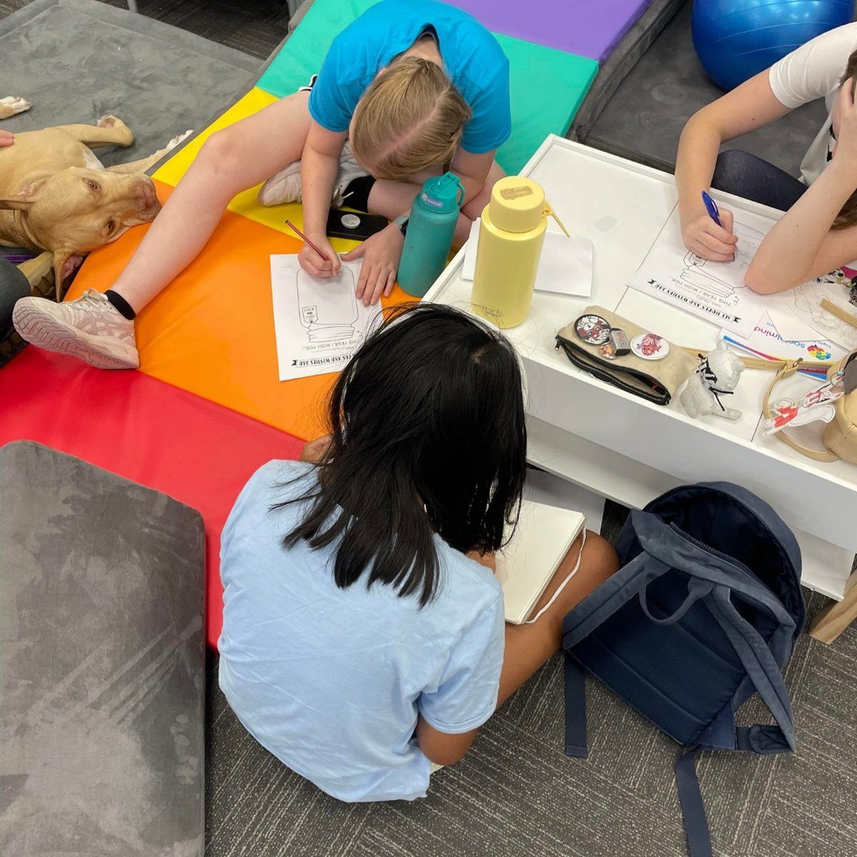 Children reading aloud beside a PAWS therapy dog