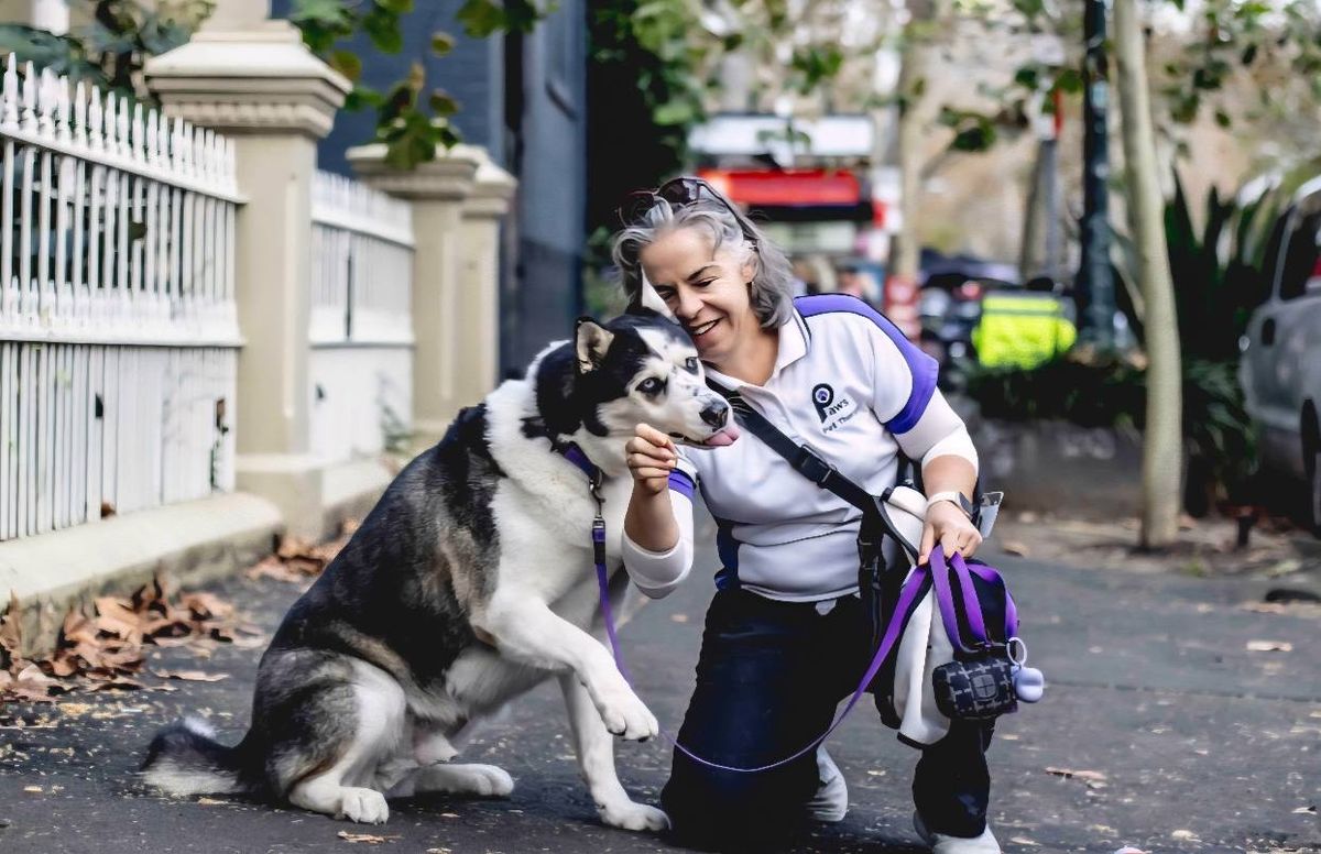 PAWS volunteer Ranelle laughing as her rescue dog Lawson jumps up for a cuddle on a city footpath
